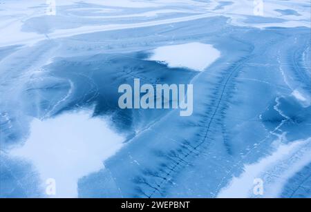 Gefrorene Seenoberfläche mit Schnee bedeckt mit Rissen im Eis. Aus der Vogelperspektive. Stockfoto