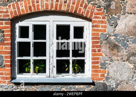 Fenster mit einem Rahmen mit alten verwitterten Farbe bedeckt, auf einer Steinmauer, in roten Ziegelsteinen gerahmt. Aus den Fenstern der Welt-Serie. Stockfoto