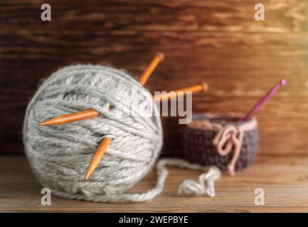 Holzstricknadeln stehen aus Garnsträngen auf hölzernem Hintergrund. Stockfoto