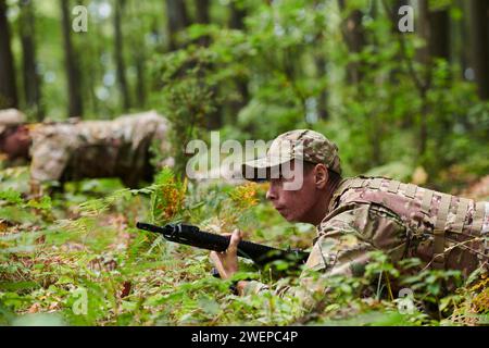 Elite-Soldaten manövrieren heimlich durch den dichten Wald, getarnt in spezieller Ausrüstung, während sie sich auf ein verdecktes und strategisches Militär begeben Stockfoto