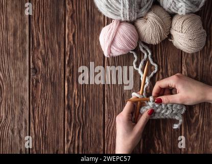 Fadenkugeln und weibliche Hände stricken sich auf einem Holztisch. Handgefertigtes Konzept. Stockfoto
