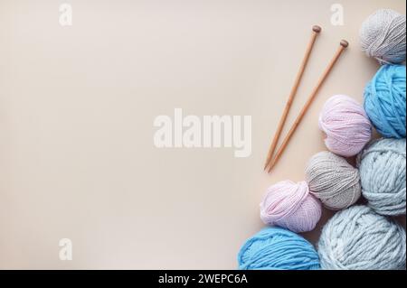 Hölzerne Stricknadeln liegen neben einem Haufen weicher Garne auf pastellfarbenem Hintergrund. Stockfoto