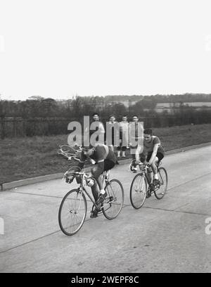 1960er Jahre, historisch, Radsport, vier männliche Zuschauer, die am Straßenrand stehen und zwei Rennradfahrer auf der Straße beobachten, die beim Amateur-Radrennen, der Daily Express Tour of Britain, England, Großbritannien, antraten. Stockfoto