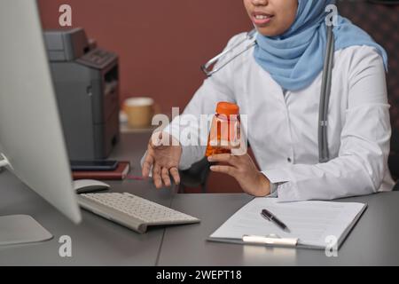 Unerkennbare junge Ärztin im Hijab, die Online-Termin mit ihrem Klienten führt Stockfoto