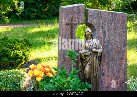 Dekoriertes Grab mit einem Grabstein mit Kreuz und der Figur „der Gute Hirte“ Stockfoto