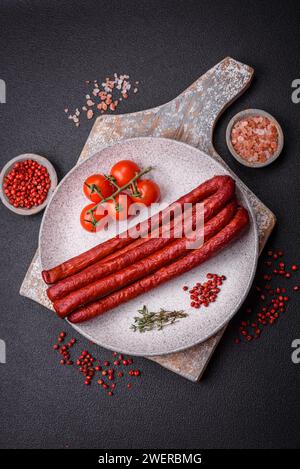 Köstliche dünne geräucherte Jagdwürste mit Salz, Gewürzen und Kräutern auf dunklem Betonhintergrund Stockfoto