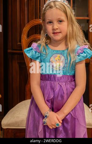 Vier Jahre altes blondes weißes Mädchen, das vor einem Stuhl steht, während es in einem Disney-Kostüm, Tinkerbell, Schmuck und Diadem gekleidet ist, während es Rollenspiele spielt. USA Stockfoto