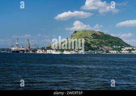 Blick auf den Hügel Morro da Penha im Stadtteil Ponta Dareia in Niteroi, umgeben von Schiffen, wie von der Guanabara Bucht unter dem sonnigen blauen Himmel am Sommernachmittag gesehen. Stockfoto