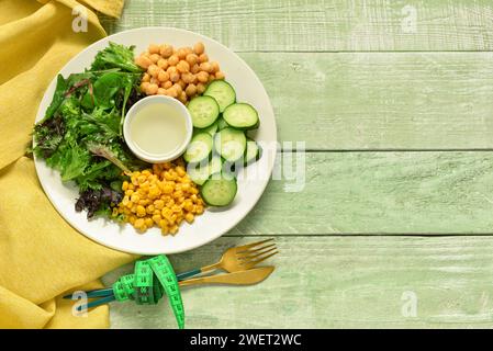 Teller mit frischem Gemüsesalat und Maßband auf grünem hölzernem Hintergrund. Diätkonzept Stockfoto
