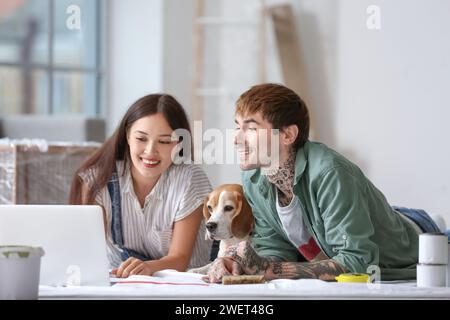 Ein junges Paar mit Beagle-Hund, der während der Reparatur in ihrem neuen Haus einen Laptop auf dem Boden benutzt Stockfoto