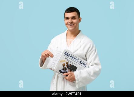 Porträt eines hübschen jungen Mannes im Bademantel mit Zeitung auf blauem Hintergrund Stockfoto