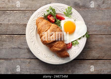 Teller mit leckerem Spiegelei, Croissant, Tomaten und Rucola auf hölzernem Hintergrund Stockfoto