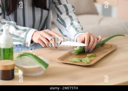 Schöne junge Frau, die Aloe Vera Blatt im Wohnzimmer schneidet, Nahaufnahme Stockfoto