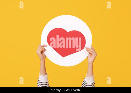 Weibliche Hände mit herzähnlichem Symbol auf gelbem Hintergrund Stockfoto