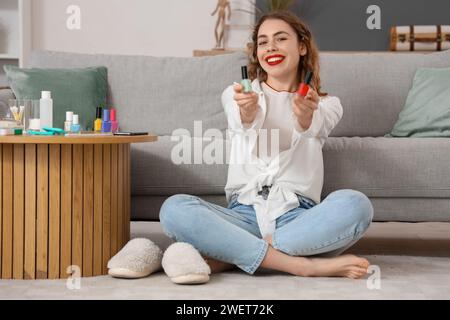 Schöne junge glückliche Frau mit Flaschen nagellack im Wohnzimmer Stockfoto