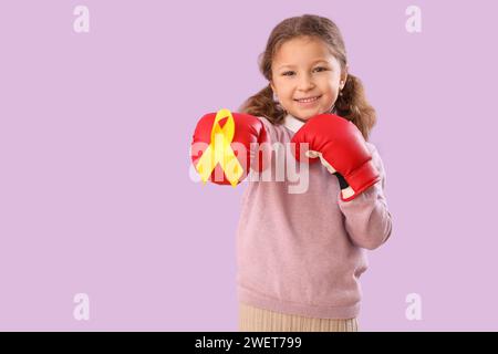 Niedliches kleines Mädchen in Boxhandschuhen mit gelbem Band auf lila Hintergrund. Krebsbewußtsein im Kindesalter Stockfoto