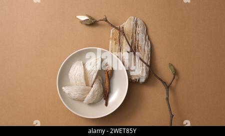 Blick von oben auf Vogelnest und Ginseng auf runder Platte, trockene Zweige und kleine Blumenzweige auf braunem Hintergrund. Werbefoto für ein teures und pr Stockfoto