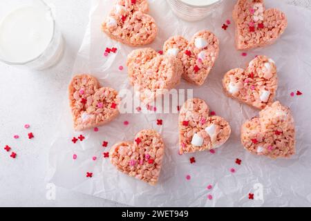 Rosafarbene herzförmige Reiskrispie-Leckereien mit Streuseln serviert mit Milch, hausgemachte süße Leckereien zum Valentinstag Stockfoto
