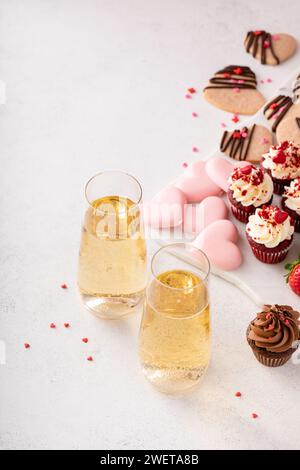 Champagner zum Valentinstag mit Dessert-Wurstplatte mit Cupcakes, Keksen, frischen Beeren und Schokolade Stockfoto