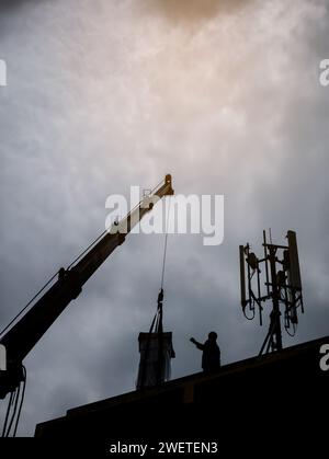 Industriekrane zum Betrieb und Anheben der elektrischen Box gegen Wolken und Himmel mit Telekommunikationsturm Stockfoto