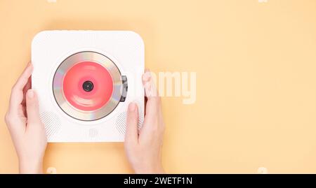 Hände halten stilvolle, tragbare, weiße CD-Player mit roter cd-Disc, die Musik auf gelbem Hintergrund wiedergibt. Retro-Disc-Player im Vintage-Stil. Oben Stockfoto