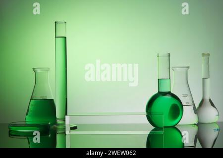 Vorderansicht des transparenten leeren Podiums, Laborausrüstung - Reagenzglas, Siedekolben, erlenmeyerkolben und Petrischale auf grünem Farbverlauf. Stockfoto