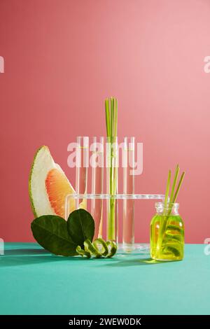 Vorderansicht der Scheiben rosa Pomelo, grüne Blätter, frisches Zitronengras und Glasflasche Zitronengras ätherisches Öl auf rosa Hintergrund. Szene für Werbung Stockfoto