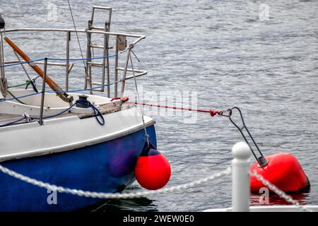 Eine rote Boje im Wasser mit dem Heck eines blauen Cutters, der am Ufer verankert ist Stockfoto