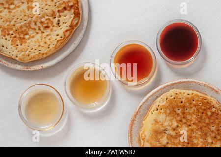 Verschiedene Klassen von Ahornsirupe in verschiedenen Farben in Glasschalen mit Pfannkuchen daneben Stockfoto