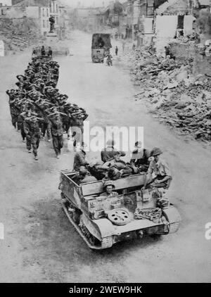 Deutsche Gefangene, die von Truppen begleitet werden, durchqueren Mitte August 1944 die Ruinen einer Stadt in der Normandie, während des Zweiten Weltkriegs nach der Invasion der Alliierten in Europa am D-Day am 6. Juni 1944. Stockfoto