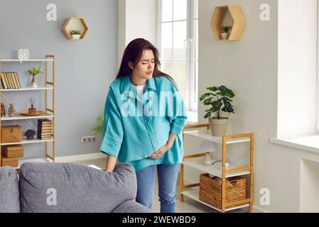 Junge Schwangere mit Wehen Schmerzen, die ihren Bauch zu Hause berühren. Stockfoto