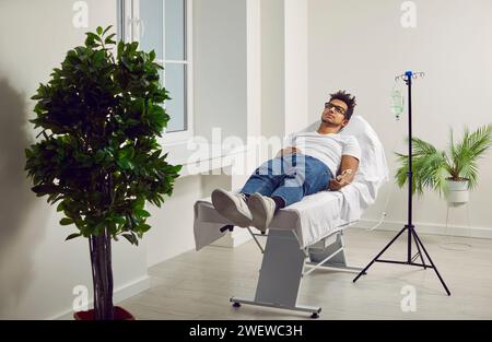 Männlicher Patient liegend im Krankenhausbett mit IV-Tropf an der Hand Stockfoto
