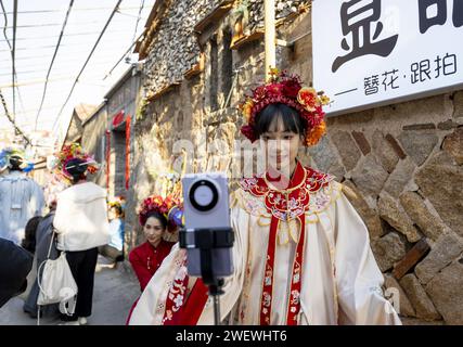 (240127) -- QUANZHOU, 27. Januar 2024 (Xinhua) -- Ein Mädchen zeigt ihre blumigen Kopfbedeckungen per Livestream im Dorf Xunpu der Stadt Quanzhou, südöstlich Chinas Provinz Fujian, 26. Januar 2024. Die blumigen Kopfbedeckungen von Xunpu, auch „Overhead Gardens“ genannt, sind eine Signatur der „Xunpu Women Customs“, die 2008 als nationales immaterielles Erbe gelistet wurde. Anfang 2023 zogen sie Millionen von Augen in der Cyber-Welt an, gefolgt von einem nachhaltigen Touristenboom im Dorf, wo Besucher buchstäblich ihre Köpfe in sie stecken können. Fotoshooting, Gastronomie und andere Dienstleistungen im Gastgewerbe haben die Quelle von in diversifiziert Stockfoto