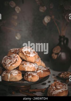 Hausgemachte Zimtbrötchen umgeben von Nüssen, Sultaninen und Zimtstangen auf dunklem Hintergrund Stockfoto