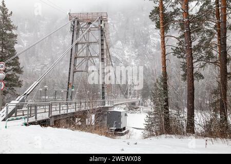 Metall-Hängebrücke für Autos und Fußgänger im Altai-Gebirge im Winter mit Schnee und Nebel auf den Bäumen ohne Menschen. Malerischer Platzgewinn Stockfoto