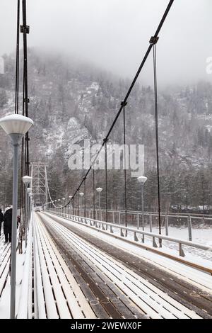 Metall-Hängebrücke für Autos und Fußgänger im Altai-Gebirge im Winter mit Schnee und Nebel auf den Bäumen ohne Menschen. Malerischer Platzgewinn Stockfoto