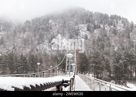 Metall-Hängebrücke für Autos und Fußgänger im Altai-Gebirge im Winter mit Schnee und Nebel auf den Bäumen ohne Menschen. Malerischer Platzgewinn Stockfoto