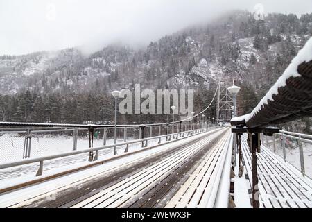 Metall-Hängebrücke für Autos und Fußgänger im Altai-Gebirge im Winter mit Schnee und Nebel auf den Bäumen ohne Menschen. Malerischer Platzgewinn Stockfoto