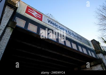 Die Eisenbahnbrücke neben dem Bahnhof in Redhill Surrey mit Welcome to Redhill Schild und britischem Eisenbahnlogo mit Straßen- und Radrouten der A25. Stockfoto