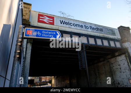 Die Eisenbahnbrücke neben dem Bahnhof in Redhill Surrey mit Welcome to Redhill Schild und britischem Eisenbahnlogo mit Straßen- und Radrouten der A25. Stockfoto