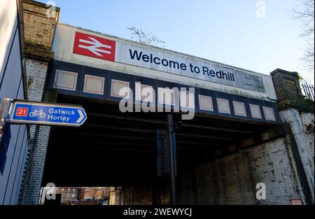 Die Eisenbahnbrücke neben dem Bahnhof in Redhill Surrey mit Welcome to Redhill Schild und britischem Eisenbahnlogo mit Straßen- und Radrouten der A25. Stockfoto