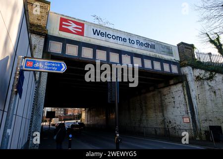 Die Eisenbahnbrücke neben dem Bahnhof in Redhill Surrey mit Welcome to Redhill Schild und britischem Eisenbahnlogo mit Straßen- und Radrouten der A25. Stockfoto