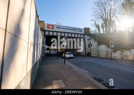 Die Eisenbahnbrücke neben dem Bahnhof in Redhill Surrey mit Welcome to Redhill Schild und britischem Eisenbahnlogo mit Straßen- und Radrouten der A25. Stockfoto