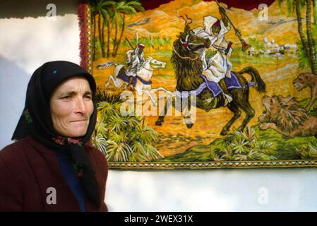 Vrancea County, Rumänien, ca. 1992. Frau in ihrem Haus, mit einem dekorativen Wandteppich, der eine Szene aus der Oper „die Entführung aus dem Serail“ von Mozart darstellt. Stockfoto
