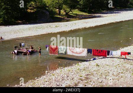 Vrancea County, Rumänien, ca. 1991. Die Einheimischen waschen Wäsche und Teppiche im Fluss Putna mit der Hand, wobei sie an einem Dock der lokalen Regierung den Wasserstand messen und die Teppiche am Kabel trocknen. Stockfoto