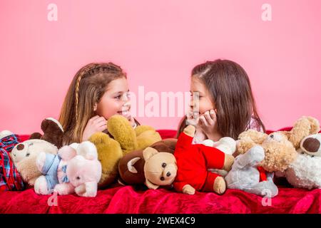 Schwestern im Pyjama liegen im Bett. Pyjama-Party. Haushaltswaren für Kinder. Kinder im weichen, warmen Pyjama, die zu Hause spielen. Mädchen in farbenfrohen Pyjamas halten lustig Stockfoto