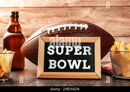 Deutschland - 27. Januar 2024: Super Bowl-Schriftzug auf einem Brett, umgeben von Snacks, Bier und einem American Football für den Super Bowl. Großes Sportereignis in Amerika FOTOMONTAGE *** Super Bowl Schriftzug auf einer Tafel umgeben von Snacks, Bier und ein American Football zum Super-Bowl. Großveranstaltung im Sport in Amerika FOTOMONTAGE Stockfoto