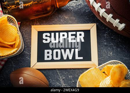 Deutschland - 27. Januar 2024: Super Bowl-Schriftzug auf einem Brett, umgeben von Snacks, Bier und einem American Football für den Super Bowl. Großes Sportereignis in Amerika FOTOMONTAGE *** Super Bowl Schriftzug auf einer Tafel umgeben von Snacks, Bier und ein American Football zum Super-Bowl. Großveranstaltung im Sport in Amerika FOTOMONTAGE Stockfoto