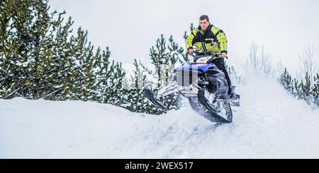 Athlet auf einem Schneemobil, der sich im Winterwald in den Bergen bewegt. Mann und schnelle Action-Schneemobil-Springen. Auf einem Schneemobil im Hintergrund springen Stockfoto