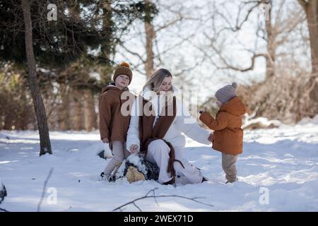 Eine aktive und fröhliche Mutter spaziert mit ihren kleinen Söhnen auf einem Pfad im Winterwald. Familienurlaub im Winter. Glückliche Mutterschaft. Stockfoto